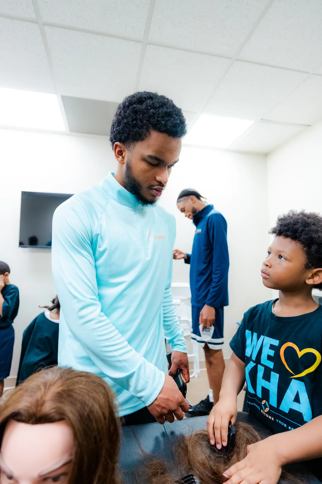 A barber mentor guiding KHA youth during the Cuts and Confidence program