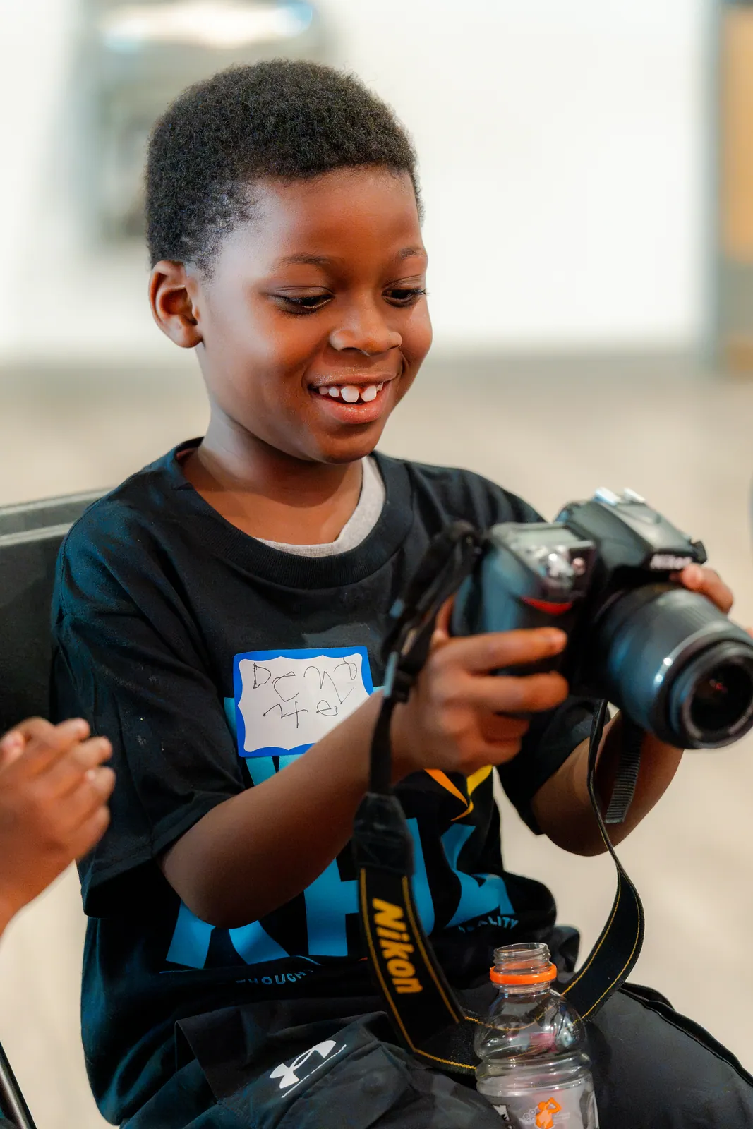 A grinning KHA youth learning to use a camera during Summer RISE