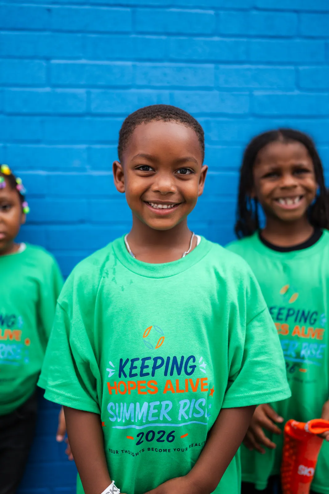 Two smiling kids in Summer RISE 2026 shirts